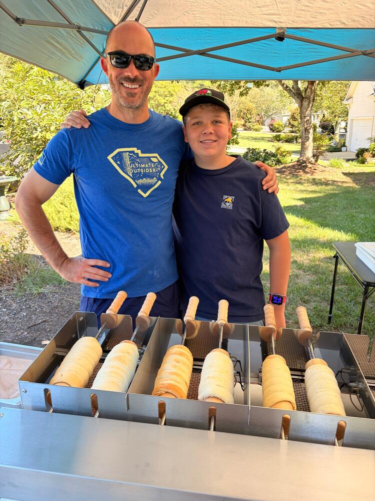 Neal and Caleb behind the rotisserie with a fresh batch of chimney cakes on the spindles